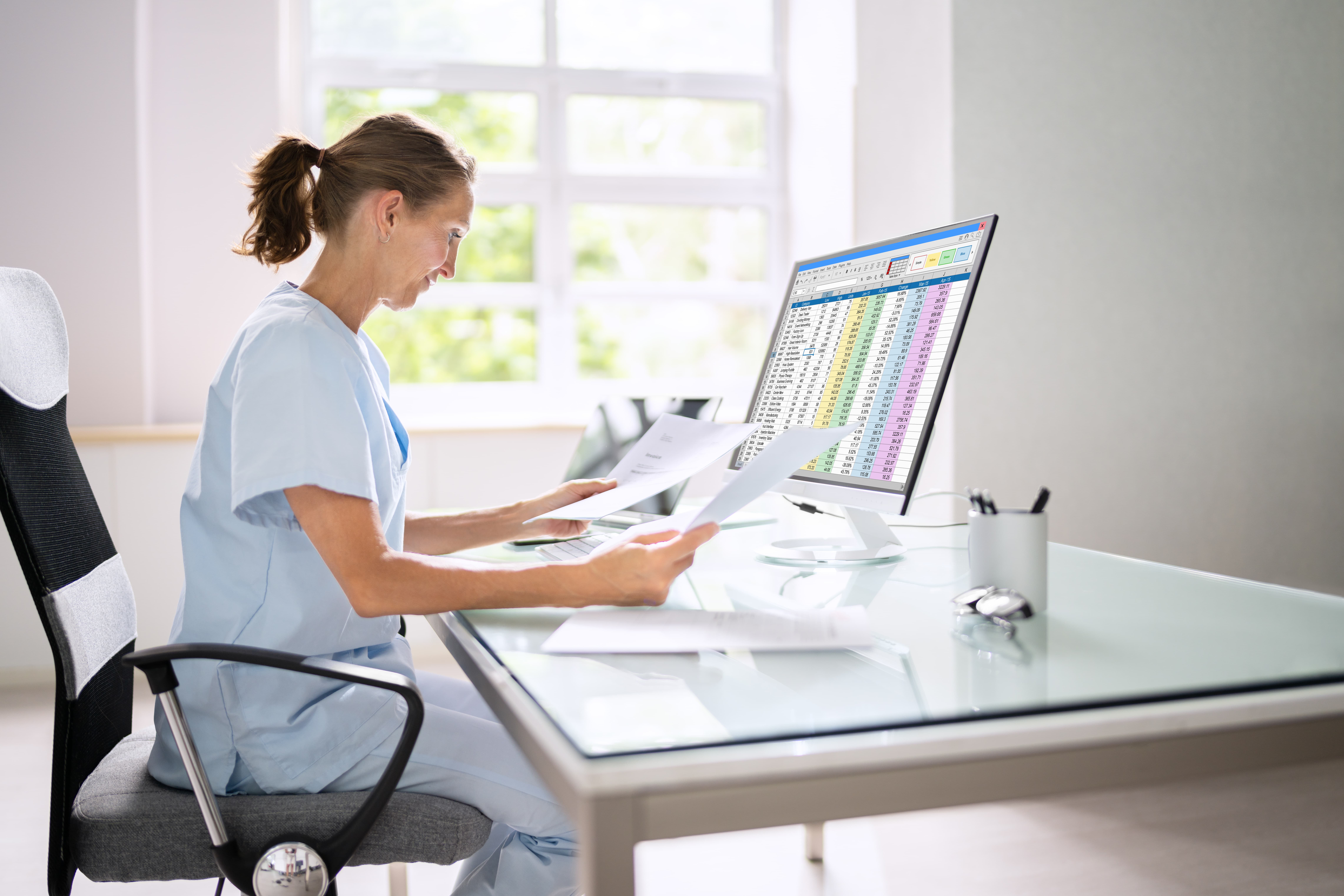 a healthcare professional looking at paperwork whilst sat at a desk, neutral tones